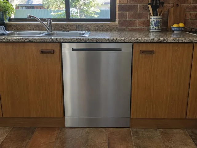 Built-in dishwasher beneath a stone benchtop in a timber kitchen with sink and window in Woodberry
