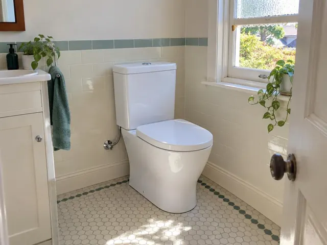 White toilet in a tiled bathroom with a window and vanity in Millers Forest
